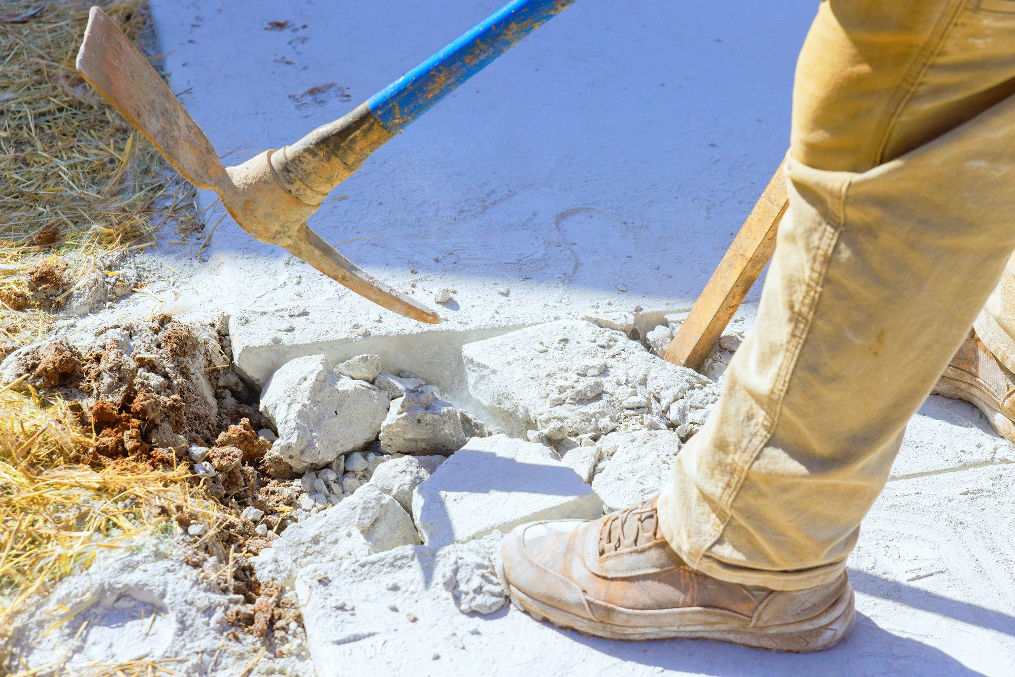 Construction site worker smashes concrete driveway with pickaxe